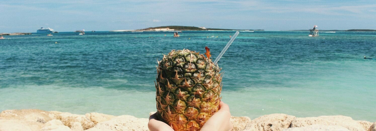 Pineapple drink held up in front of the beach