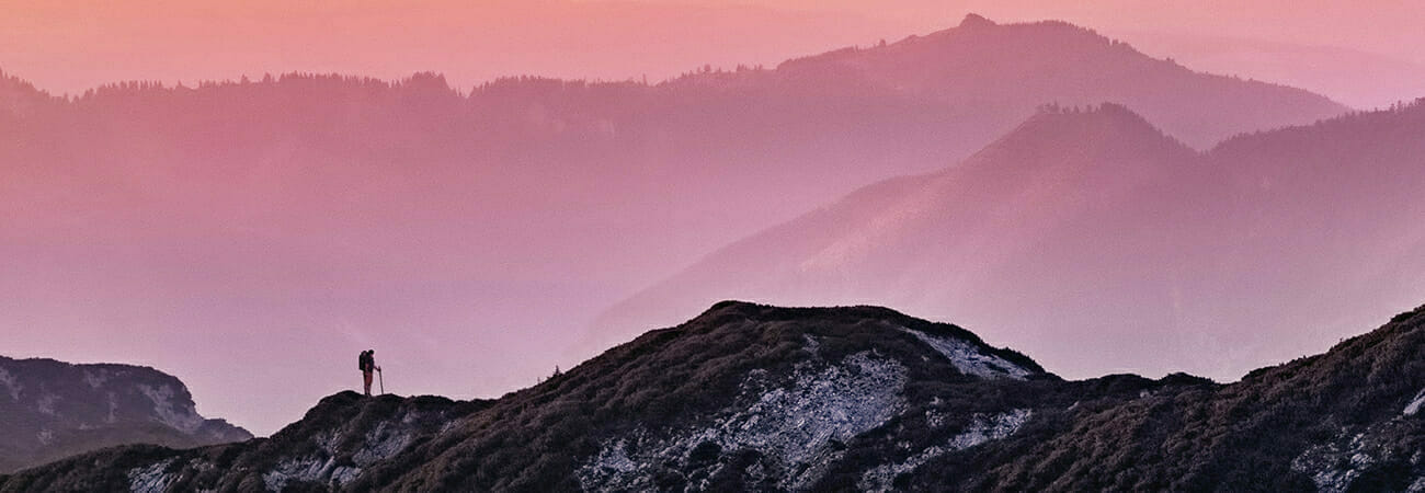 Person hiking on mountain against pinkish sky