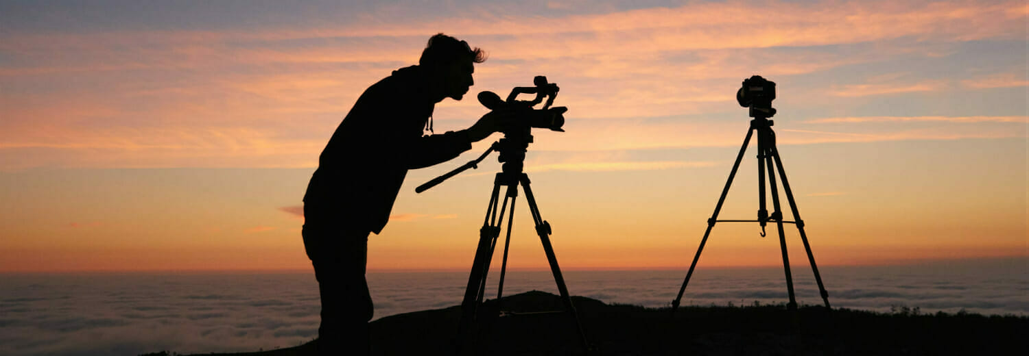Person with camera on tripod on hill at sunset