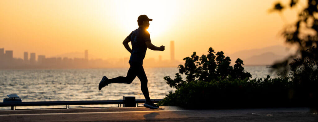 A silhouette of a person jogging by the water at sunset