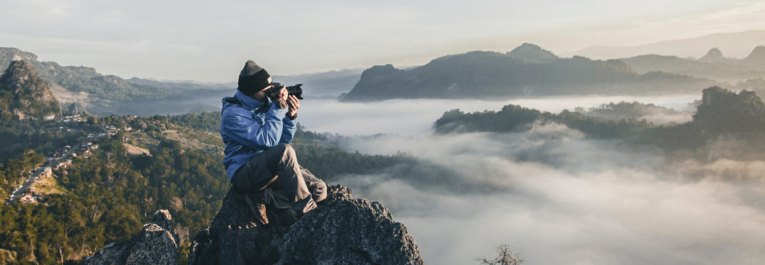 Man taking photo on edge of mountain above the clouds